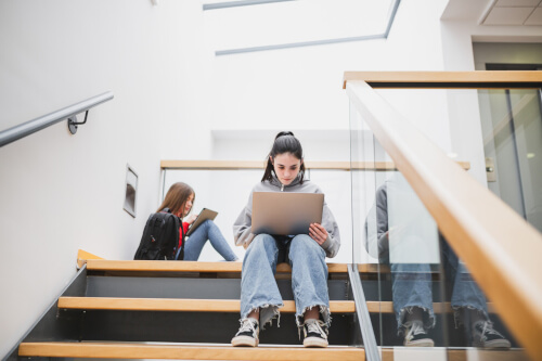 school child on stairs in school on laptop