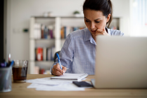 woman writing a report with notepad and pc